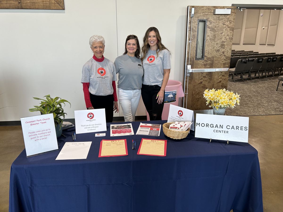 Three Morgan Cares Center volunteers standing behind an information table at Covenant Park Church.