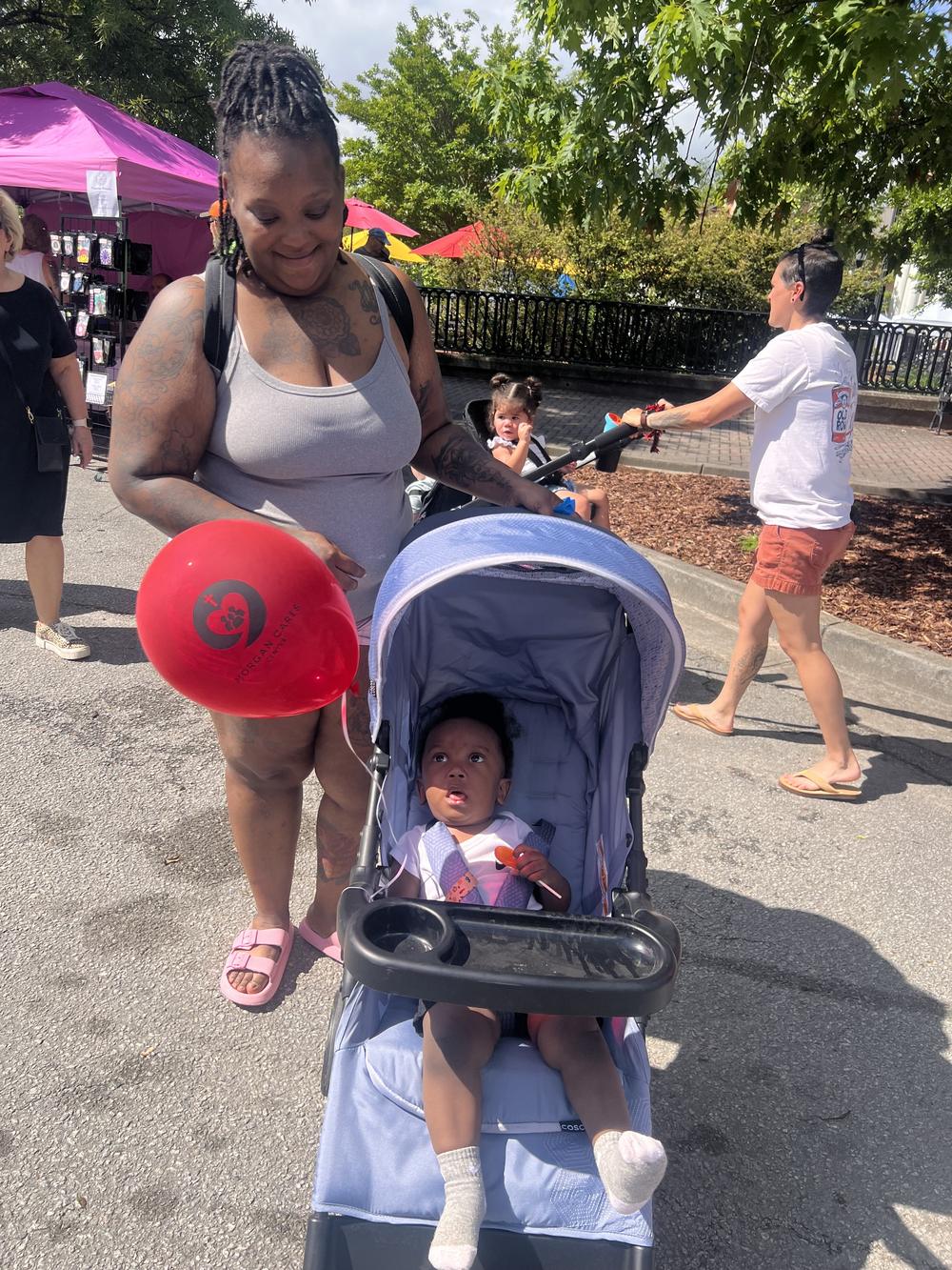 A mother walks through a community festival with a red Morgan Cares Center balloon.
